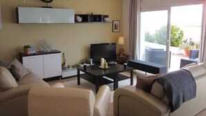 Een woonkamer met een bank, een salontafel, een televisie en een balkon met planten.