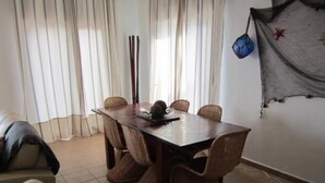 Een eetgedeelte met een tafel en stoelen, een raam met gordijnen, en een wand met een decoratief object.