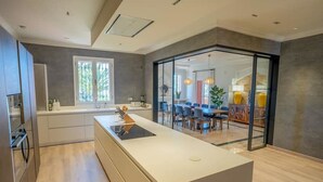 A modern kitchen with a central island, a dining area with chairs, and a large window.