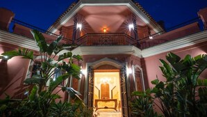 A building with a balcony, a central entrance, and surrounding greenery.