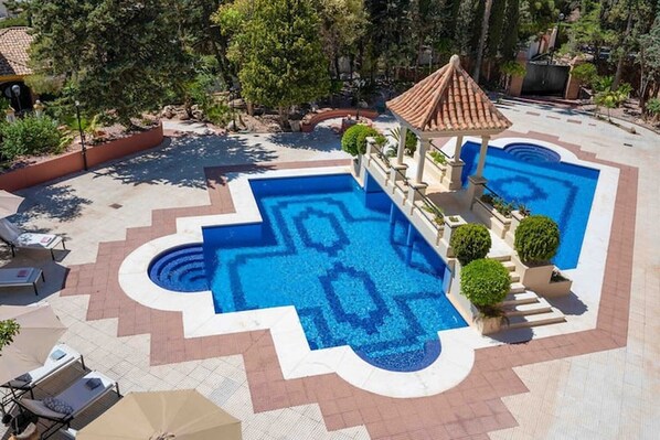 A swimming pool with geometric tile patterns, surrounded by lounge chairs and a covered seating area.
