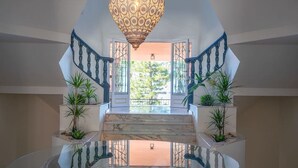 A grand staircase with a marble floor, a decorative hanging light fixture, and potted plants.