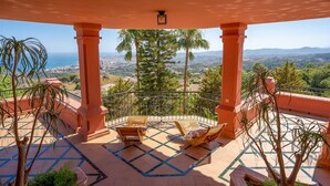 A balcony with a view of a cityscape, palm trees, and a tiled floor.