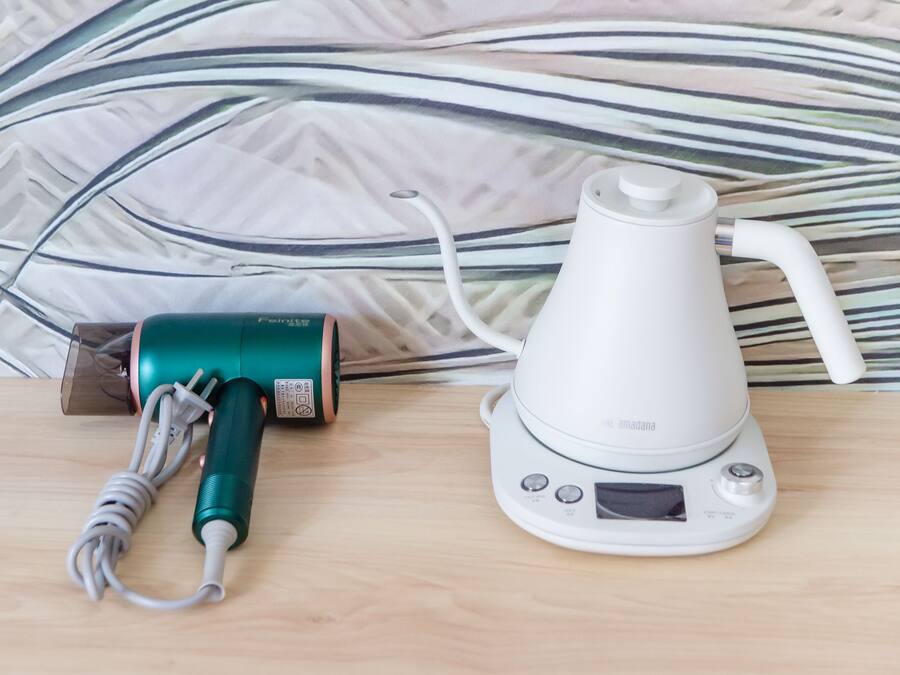 Un assecador i una olla elèctrica sobre una superfície de fusta amb una paret decorada al fons.