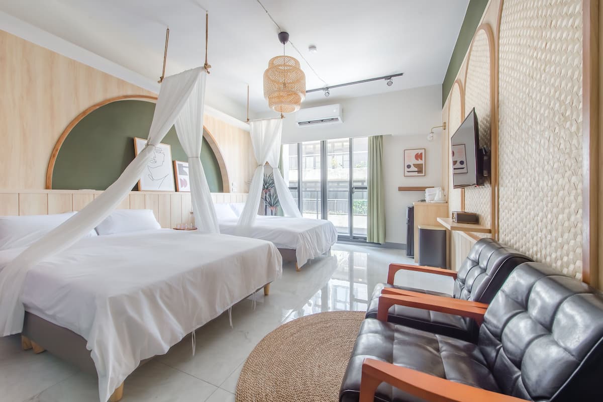 A hotel room with two beds, a sofa, a woven rug, a television, and a wall-mounted air conditioning unit.