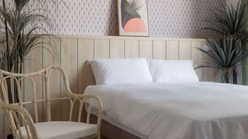 Quarto com cama, duas almofadas brancas, cabeceira de madeira, cadeira de vime e duas plantas em vasos.