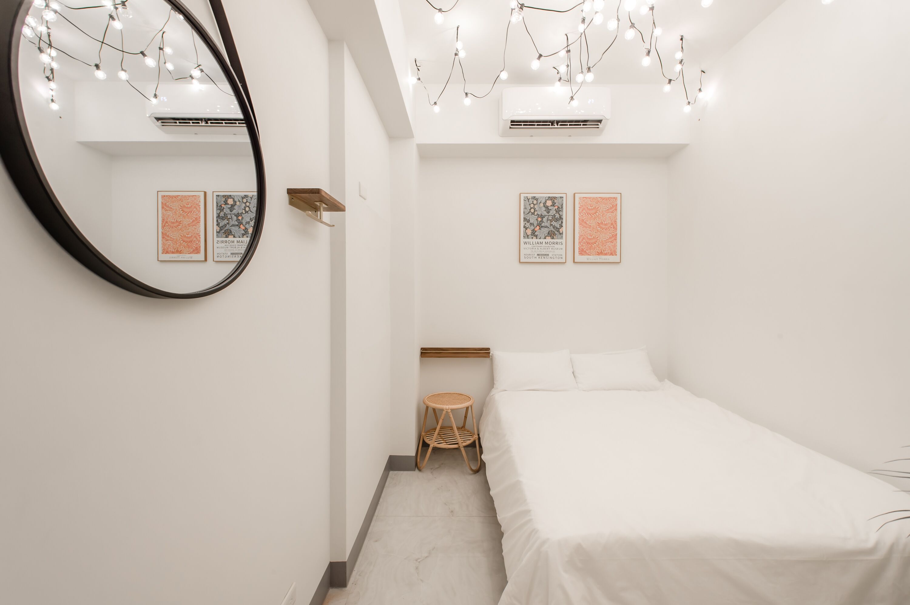 Un dormitorio minimalista con una cama, un espejo redondo y dos cuadros enmarcados en la pared.