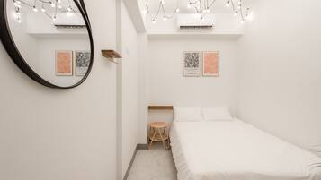 Un dormitorio minimalista con una cama, un espejo redondo y dos cuadros enmarcados en la pared.