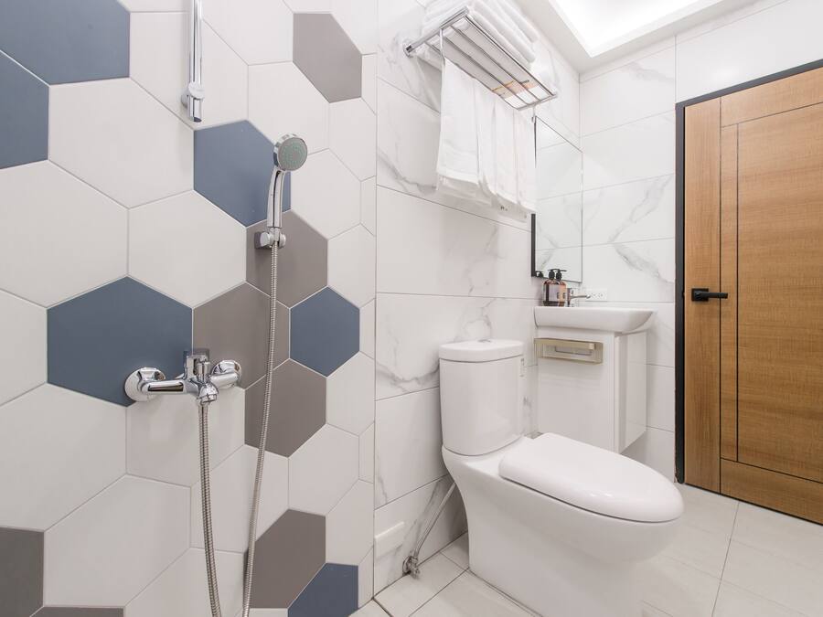 Casa de banho moderna com chuveiro, sanita e lavatório, com azulejos hexagonais e porta de madeira.