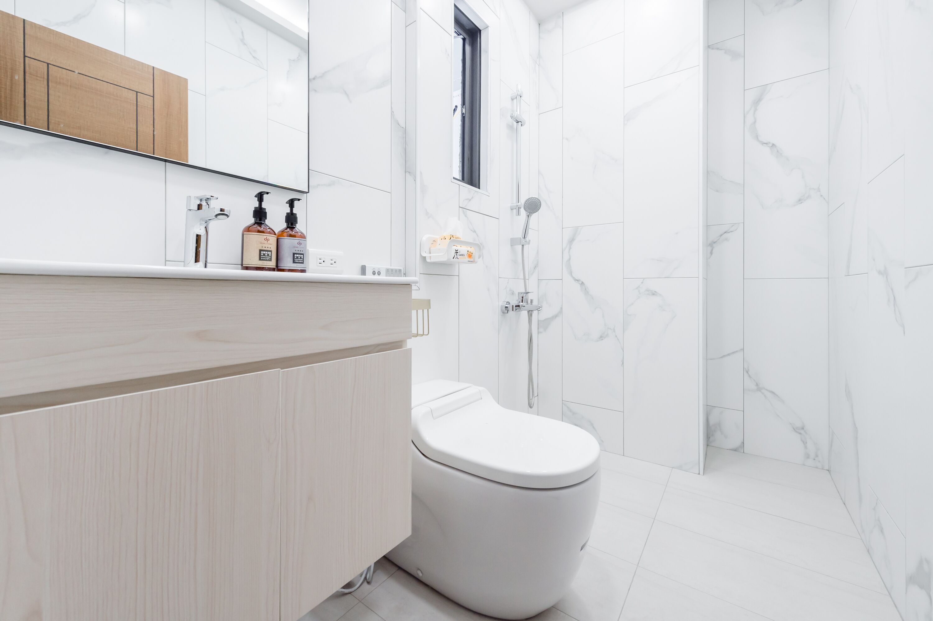 A modern bathroom with a white toilet, a wooden vanity, and a shower area.