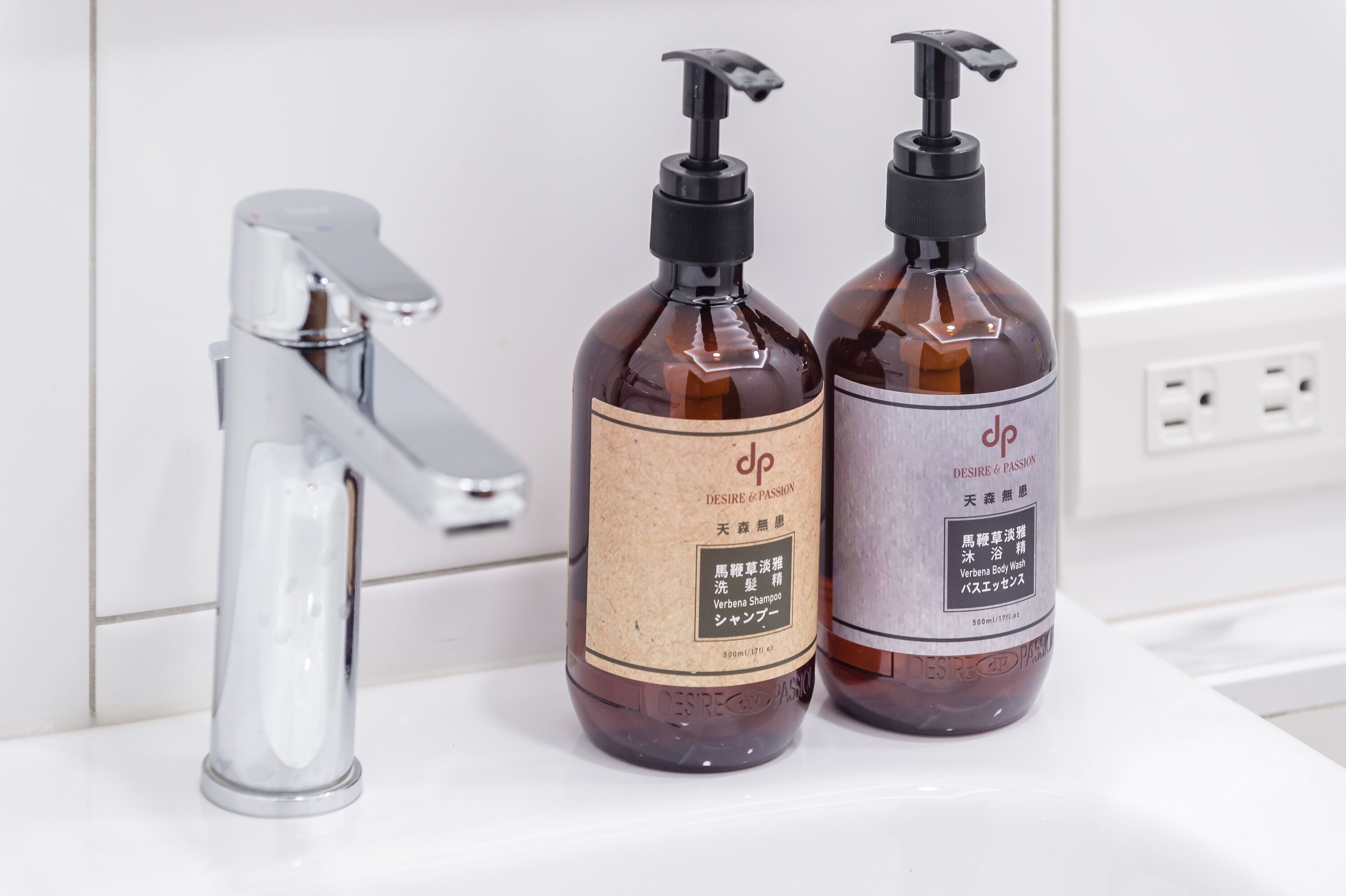 Zwei Flaschen Shampoo und Conditioner auf einer weißen Oberfläche mit einem chromfarbenen Wasserhahn.