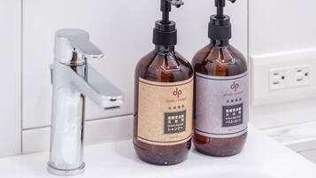 Zwei Flaschen Shampoo und Conditioner auf einer weißen Oberfläche mit einem chromfarbenen Wasserhahn.