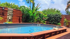 A wooden deck surrounding a rectangular pool with a stone face sculpture on the left.