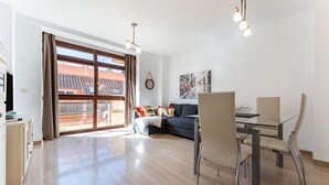 Ett modernt vardagsrum med en soffa, ett matbord, stolar, en tv och ett stort fönster med gardiner.