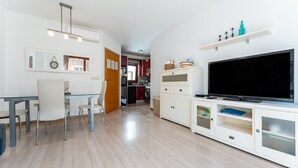 Ett modernt vardagsrum med en platt-TV, en matplats med stolar, ett kök i bakgrunden och en tvättstuga.
