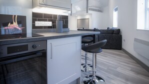 Una cocina moderna con horno integrado, una barra con taburetes y una sala de estar con sofá.