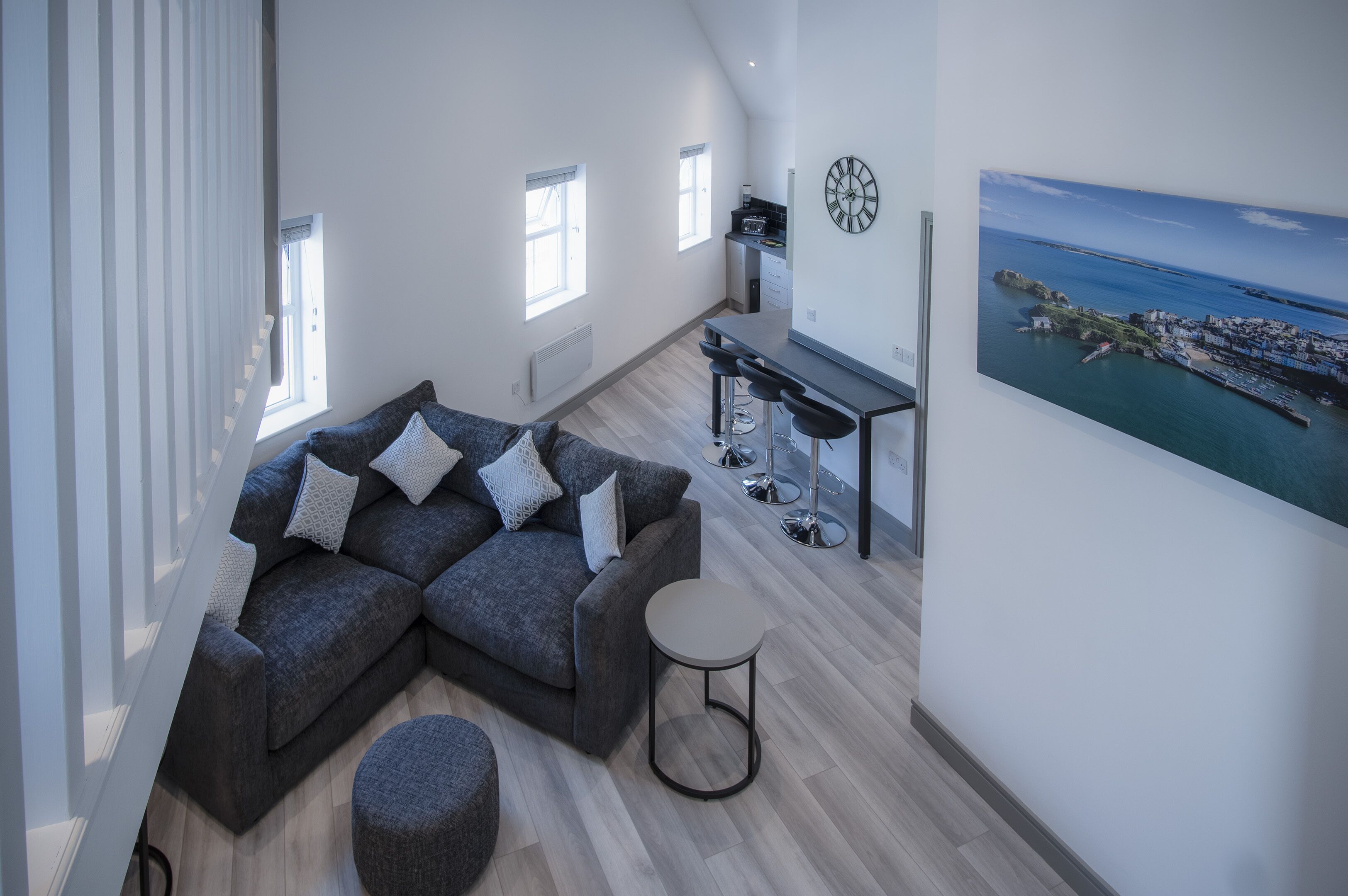 A modern living room with a gray sectional sofa, a round coffee table, and a view of the kitchen and dining area.