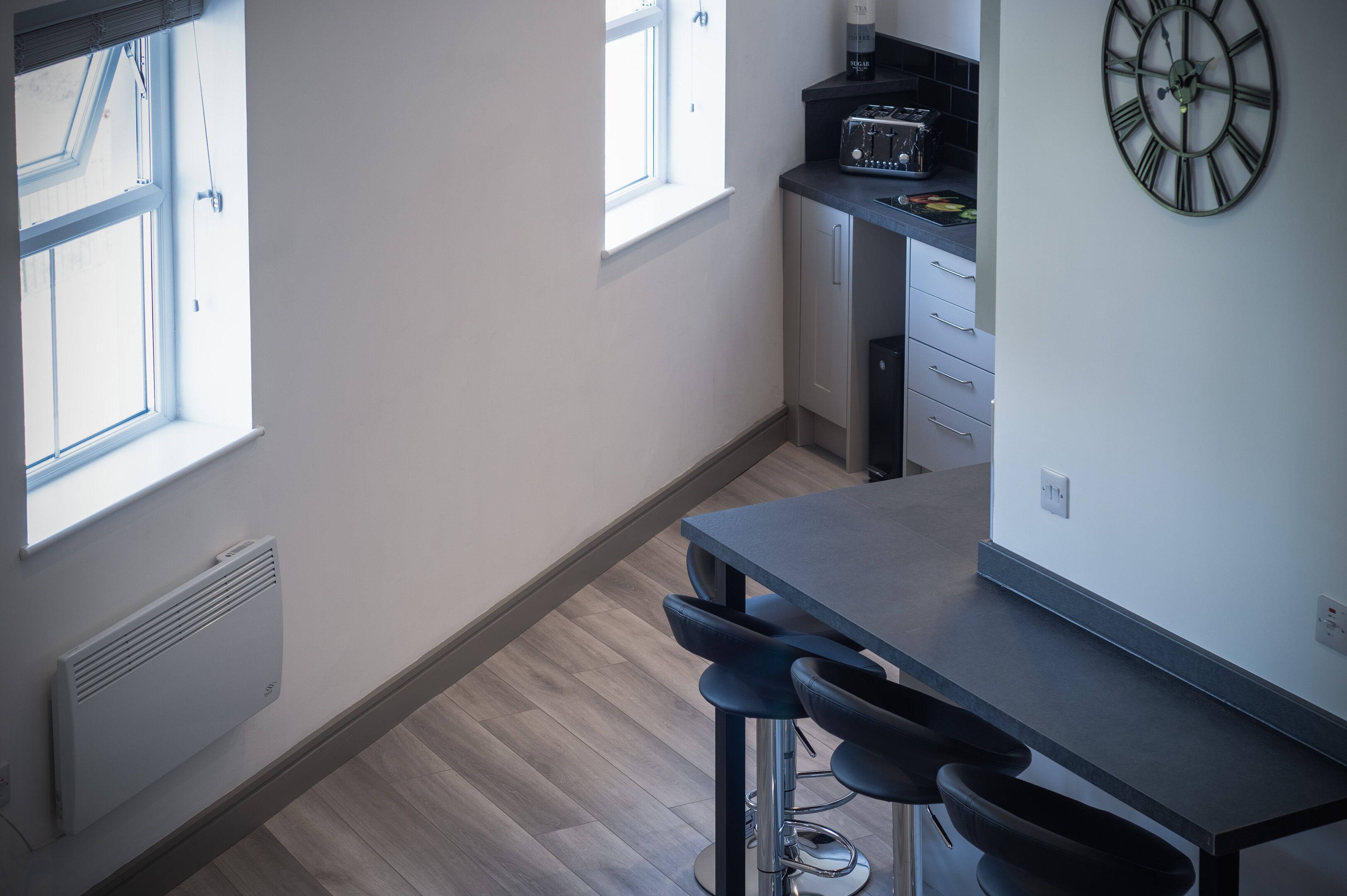 A modern kitchen with a window, a clock, and a bar stool.