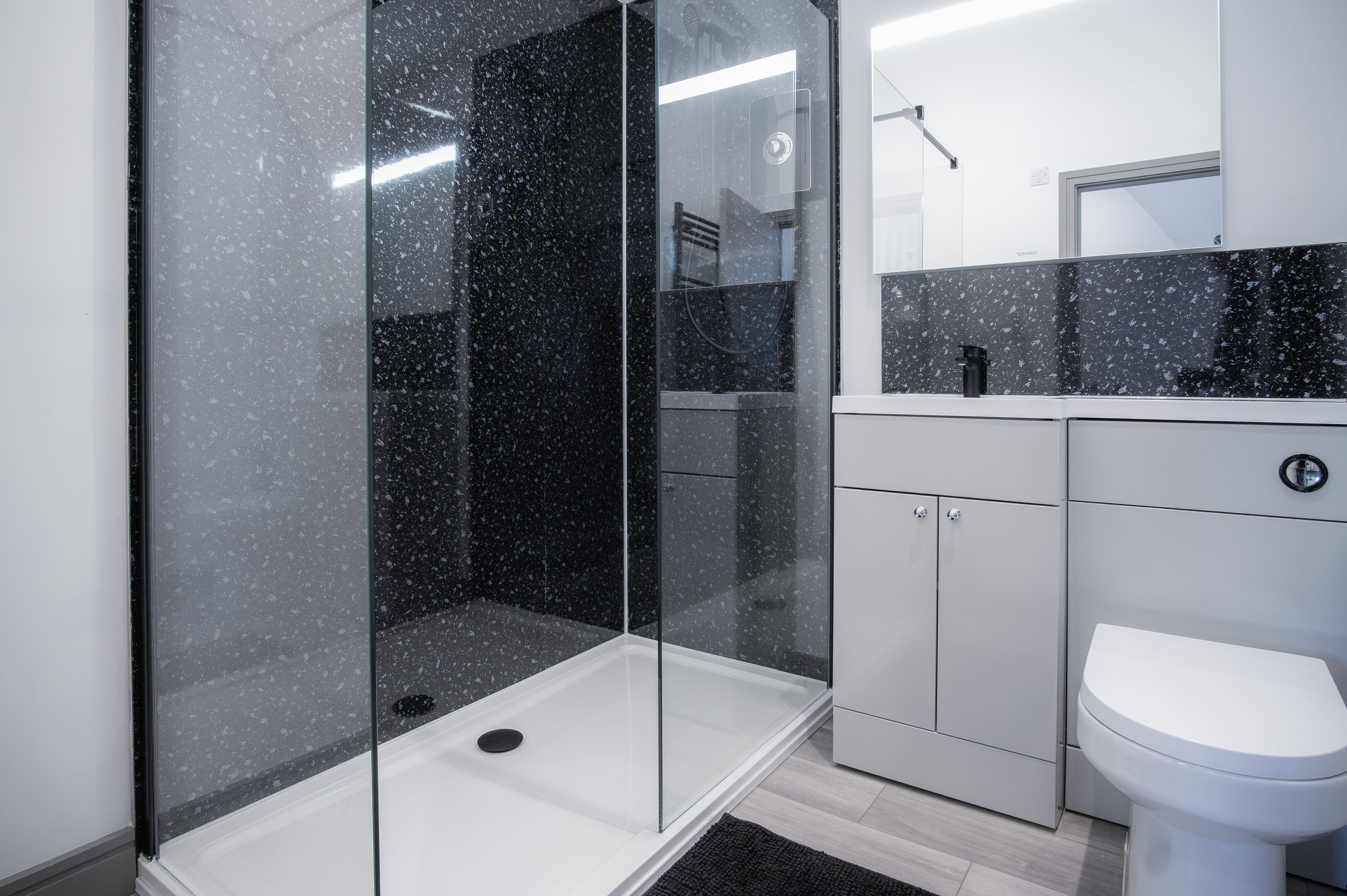 A modern bathroom with a glass-enclosed shower, a white toilet, and a grey cabinet.