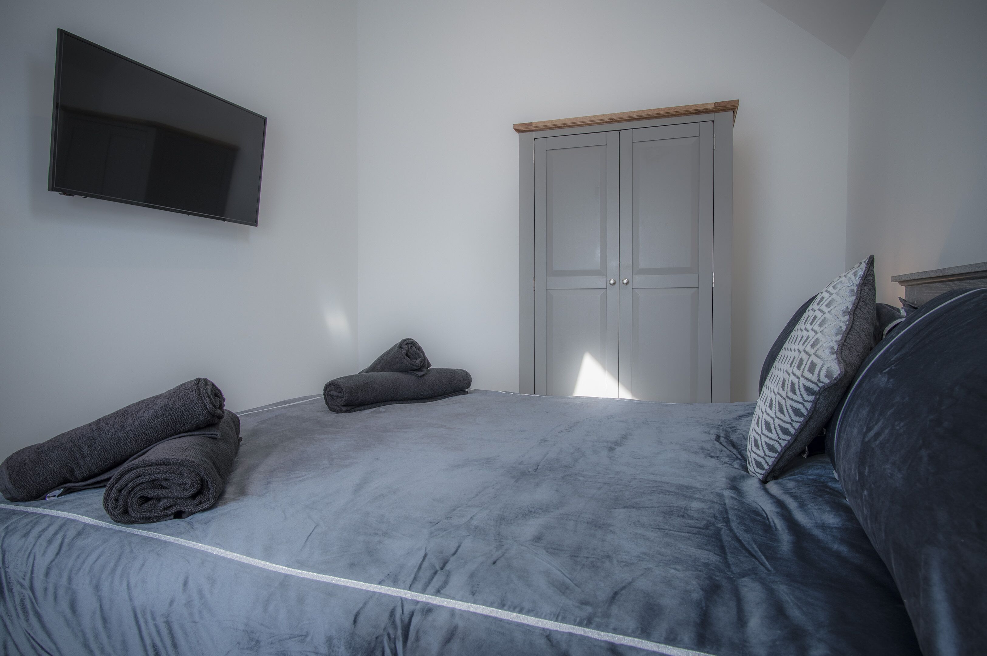 A bedroom with a bed, a wardrobe, and a flat-screen TV mounted on the wall.