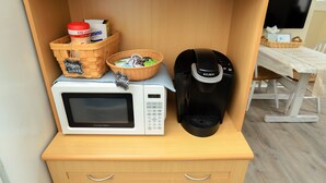 Une petite cuisine équipée d’un four à micro-ondes, d’une machine à café et de paniers étiquetés « crème et sucre » et « café ».