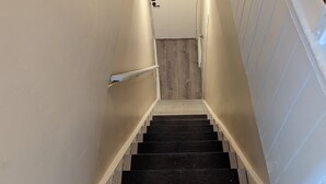 Un escalier avec des marches en bois et une rampe, menant à une porte dotée d’un interrupteur et d’une serrure.