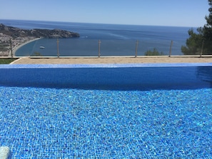 A pool with clear blue water, a sandy beach, and a view of the ocean.