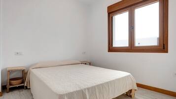 A bedroom with a bed, a small wooden nightstand, a window, and a light switch on the wall.