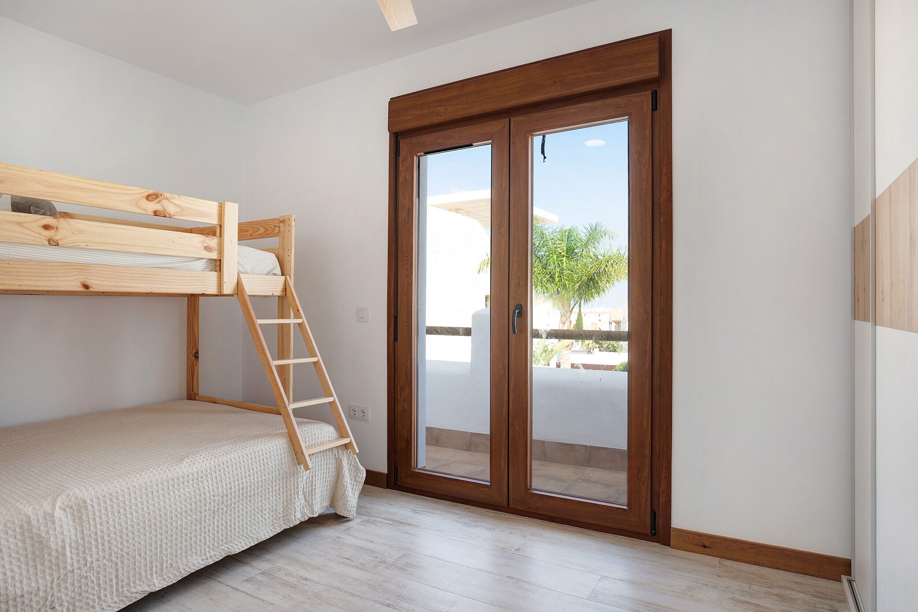 Quarto com beliche, escada de madeira, porta de vidro deslizante e vista para o exterior.