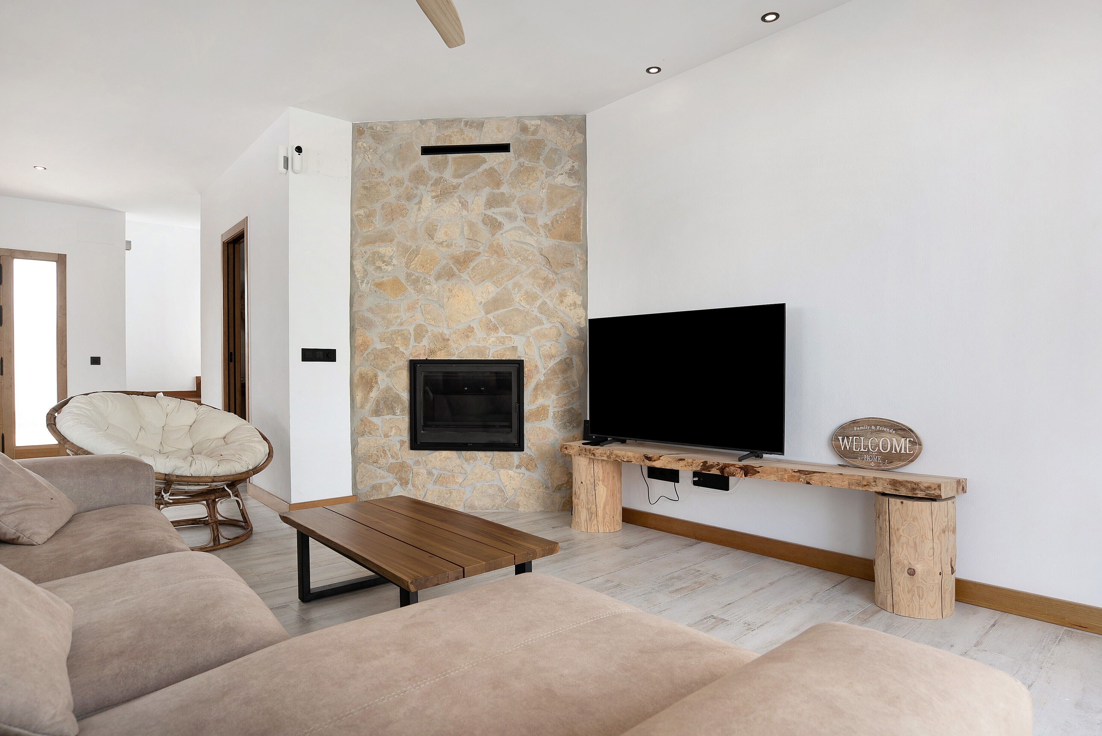 Uma sala de estar moderna com parede de pedra, televisão de tela plana, mesa de centro de madeira e uma cadeira de vime.