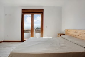 A bedroom with a bed, wooden headboard, a nightstand, a window with a view, and a door.