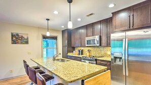 A modern kitchen with dark wooden cabinets, a stainless steel refrigerator, a granite countertop, and a bar area with stools.