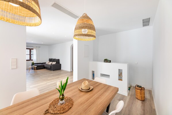 Un salon moderne avec un canapé, une table à manger agrémentée d’un vase et d’une plante, et un luminaire suspendu.