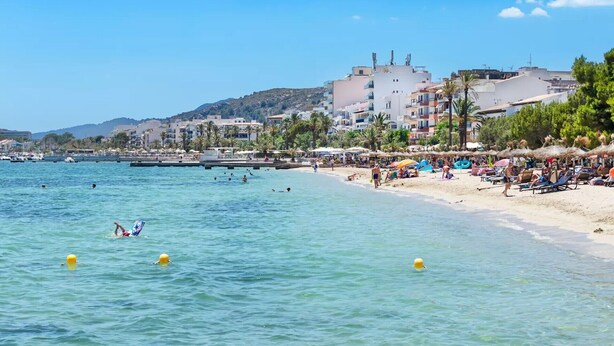 A beach with clear water, umbrellas, and people. - Apartment 'Albercutx Pollentia 1' with Terrace, Air Conditioning and Wi-Fi (Puerto de Pollensa)
