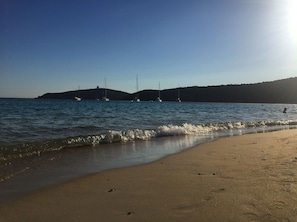Ein Strand mit ruhigem Wasser, Booten und einer hügeligen Landschaft im Hintergrund.
