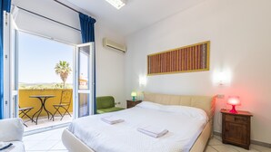 Ein Hotelzimmer mit Bett, Tisch mit Stühlen, Lampe und Blick ins Freie.