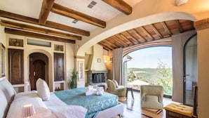 Un dormitorio con cama, televisor, chimenea, vistas al exterior y vigas de madera en el techo.