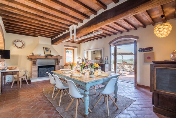 A dining area with a wooden table, chairs, a fireplace, and a view of the outdoors.