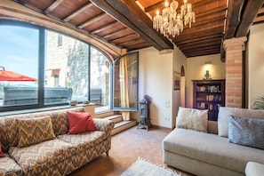 Una sala de estar acogedora con un sofá, un sillón adicional, una estantería y un ventanal grande.