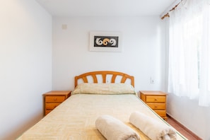 Un dormitorio con una cama, dos mesitas de noche de madera, una obra de arte colgada en la pared y una ventana con cortinas.