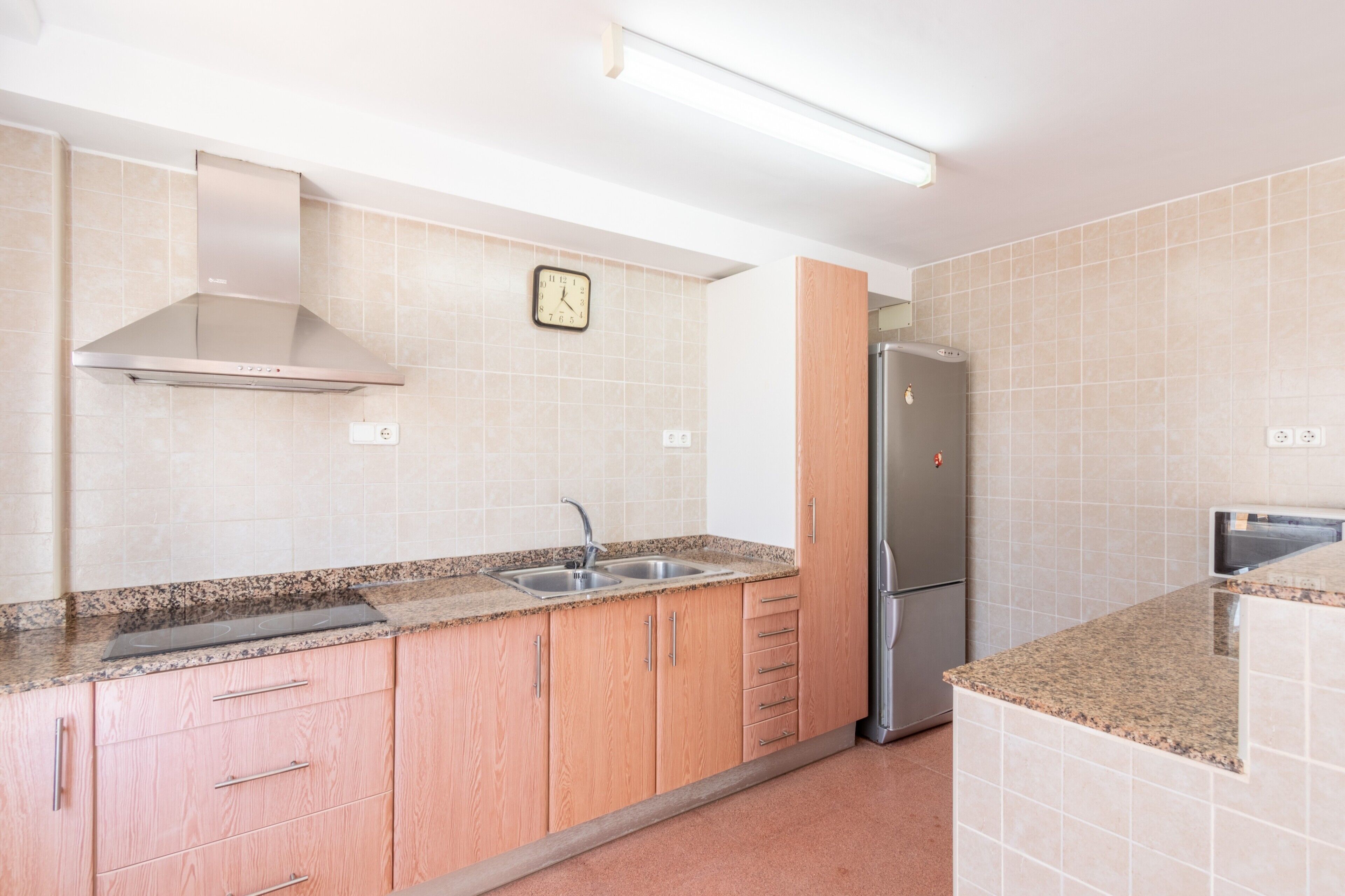 A kitchen with a stainless steel range hood, a sink, a clock, and a refrigerator.