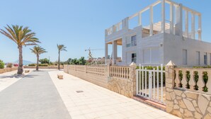 Un bâtiment moderne à la façade blanche, doté d’une entrée sécurisée et d’un chemin piétonnier dallé bordé de palmiers.