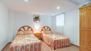 Une chambre avec deux lits, une armoire en bois, une table de chevet avec une lampe et un tableau encadré au mur.