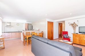 Un espacio habitable moderno con comedor, sofá, televisor y cocina al fondo.