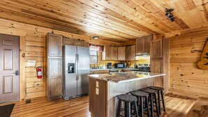 A wooden cabin-style kitchen with a central island, bar stools, a refrigerator, microwave, and a stove.