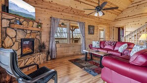 A cozy cabin interior with a stone fireplace, leather sofa, and a large TV.