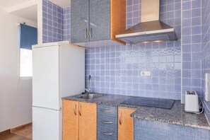 A kitchen with blue tiles, a white refrigerator, wooden cabinets, a stainless steel range hood, and a toaster.