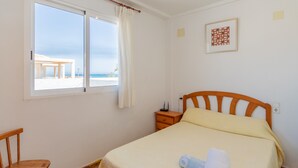 Un dormitorio con cama, mesita de noche, silla, ventana con cortinas e imagen enmarcada en la pared.