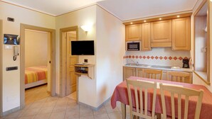 Une pièce compacte comprenant un lit, un téléviseur, un petit coin cuisine et une table à manger avec des chaises.