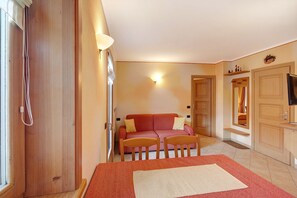 A room with a wooden door, a red sofa, a wooden chair, a small table, and a television.